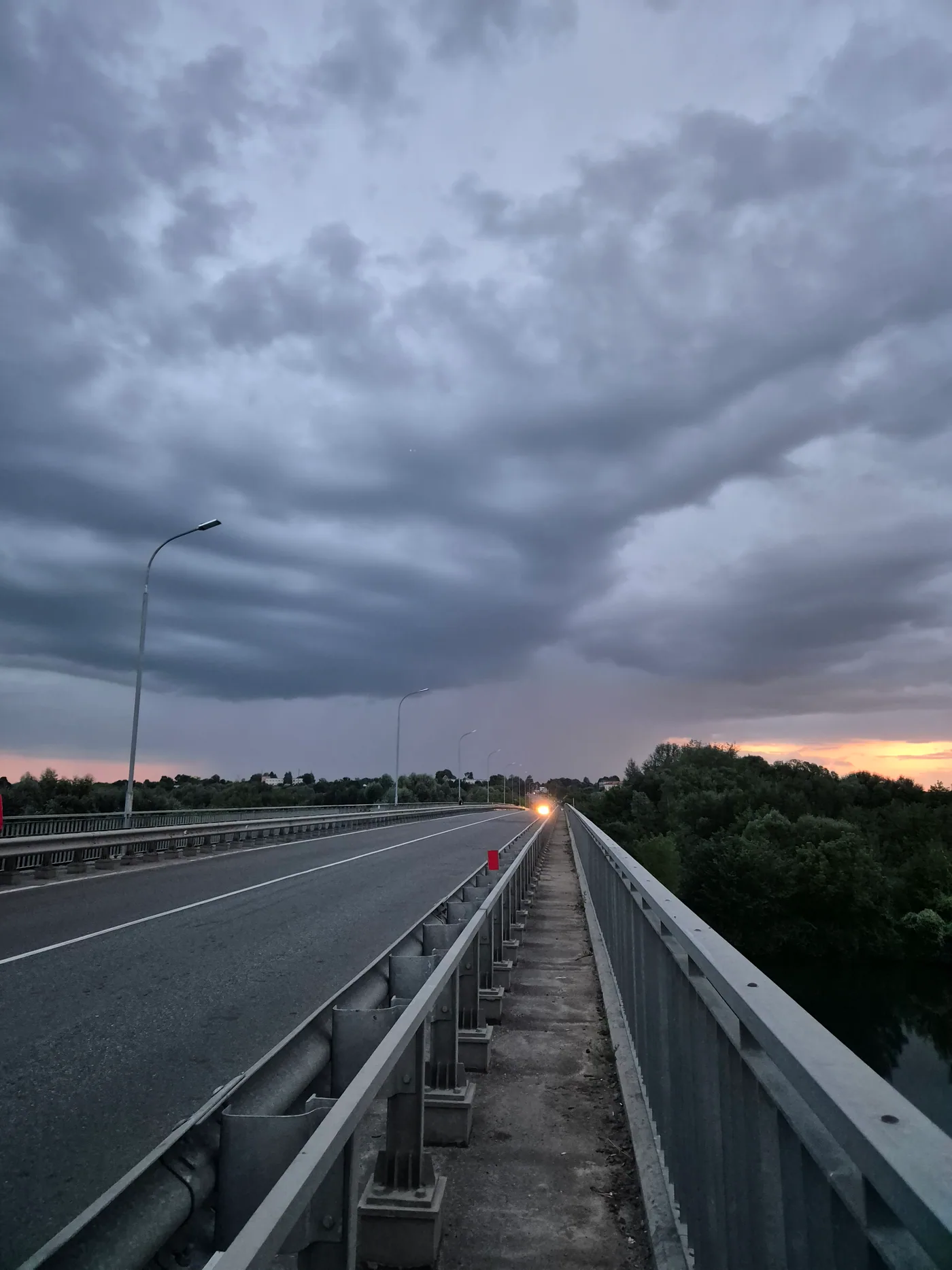 An empty bridge leading toward dark storm clouds